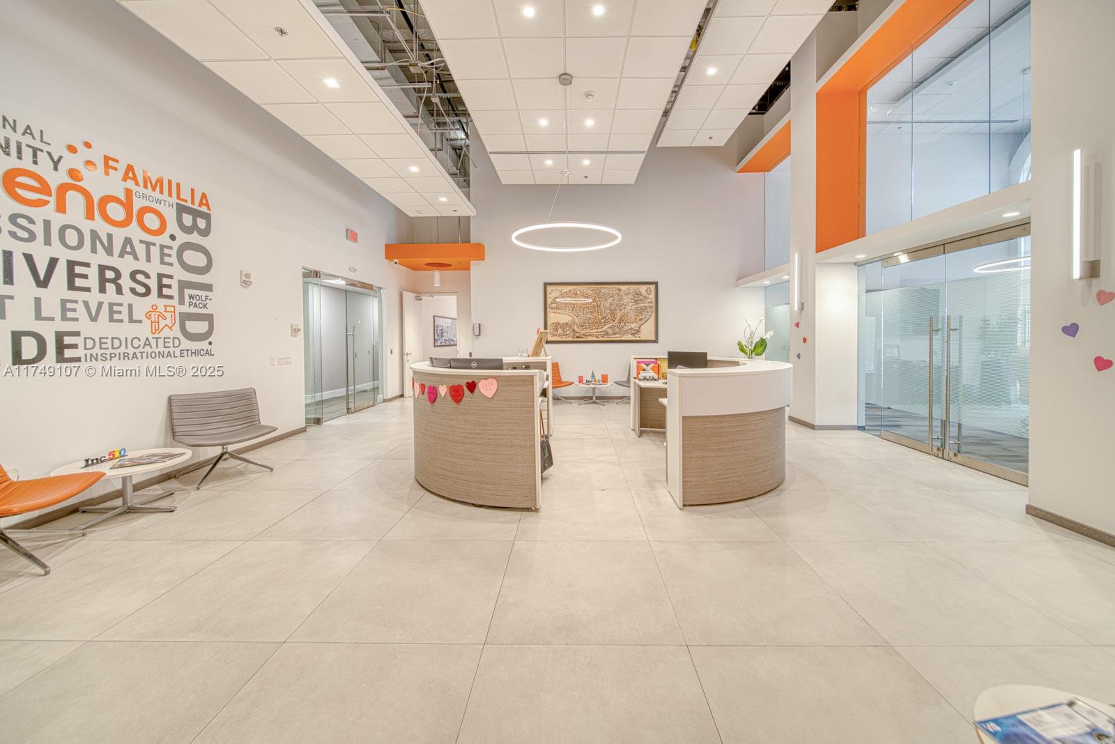 A modern office reception area features two curved desks, tile flooring, and a high ceiling — 2 Alhambra Plz # A, Coral Gables FL 33134, CORAL GABLES, FL