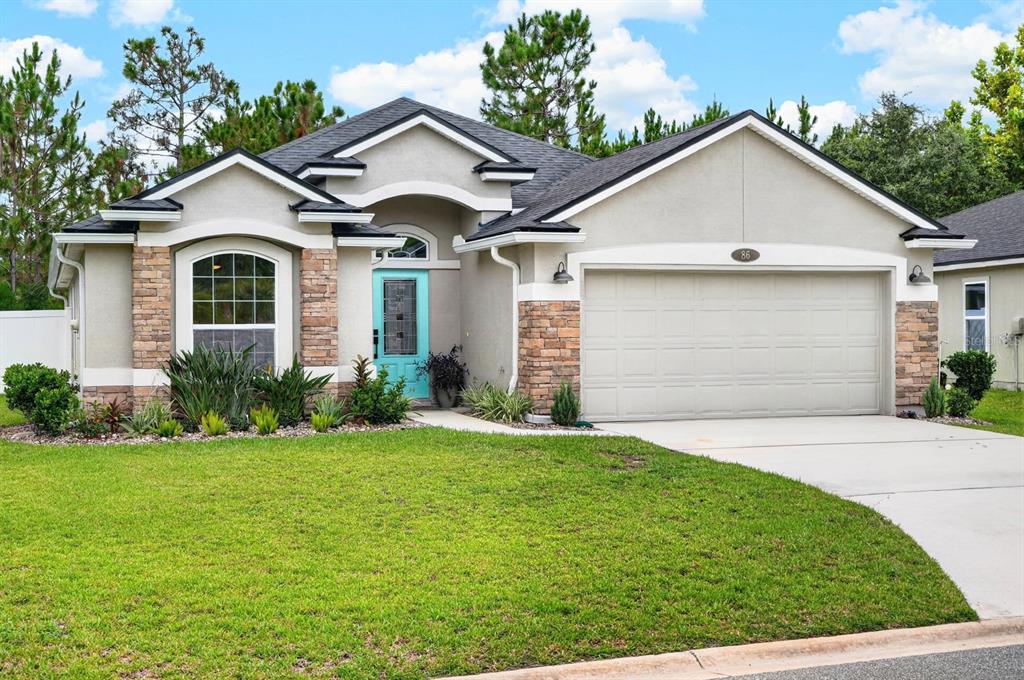 A single-story house with a beige stucco exterior, stone accents, and a turquoise front door — 86 LITTLE OWL LANE, ST AUGUSTINE, FL