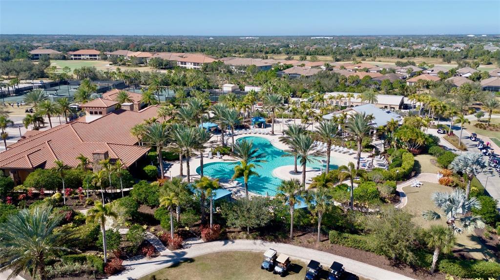 An aerial view shows a resort-style swimming pool surrounded by palm trees and a clubhouse — 13218 TORRESINA TERRACE, BRADENTON, FL
