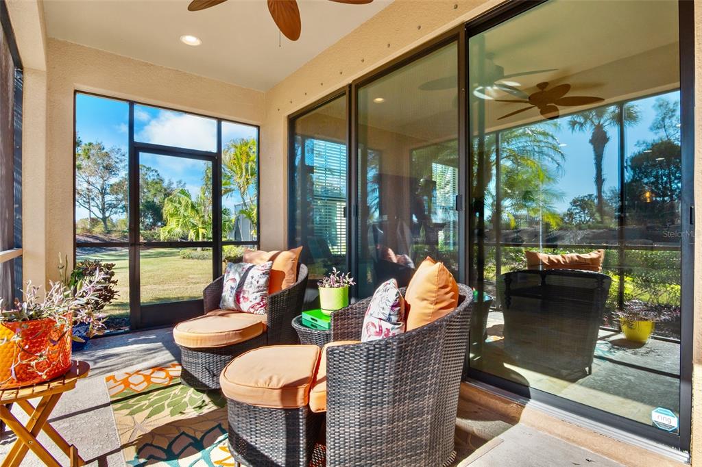 A screened-in patio features wicker chairs, orange cushions, and large sliding glass doors — 13218 TORRESINA TERRACE, BRADENTON, FL