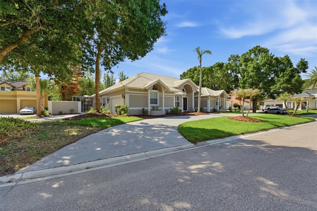 A beige single-story house with a concrete driveway and mature trees in a suburban neighborhood — 8935 JONATHAN MANOR DRIVE, ORLANDO, FL