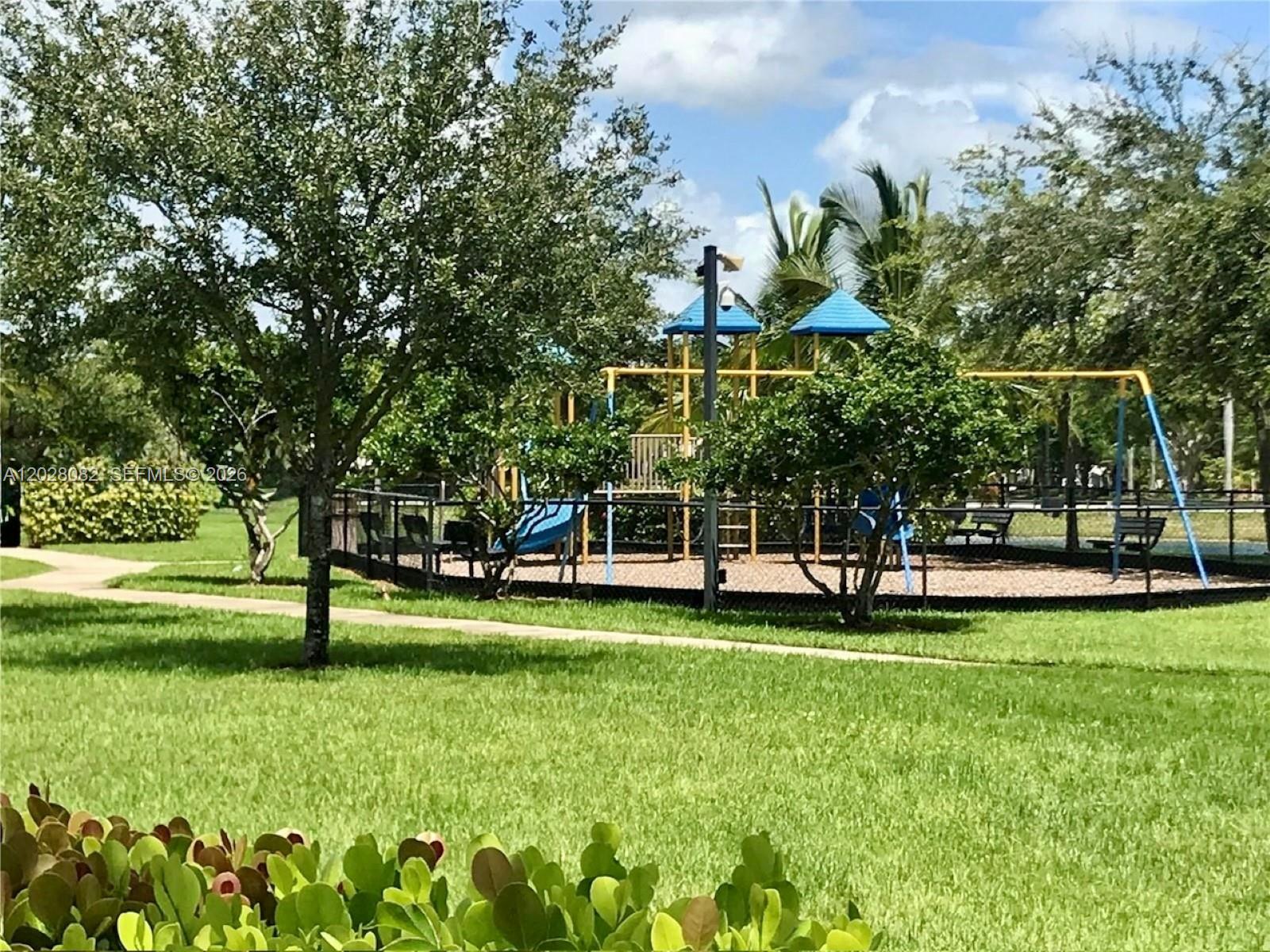 A fenced playground with a play structure sits in a grassy park with trees — 22541 SW 88th Pl # 6, Cutler Bay FL 33190, CUTLER BAY, FL