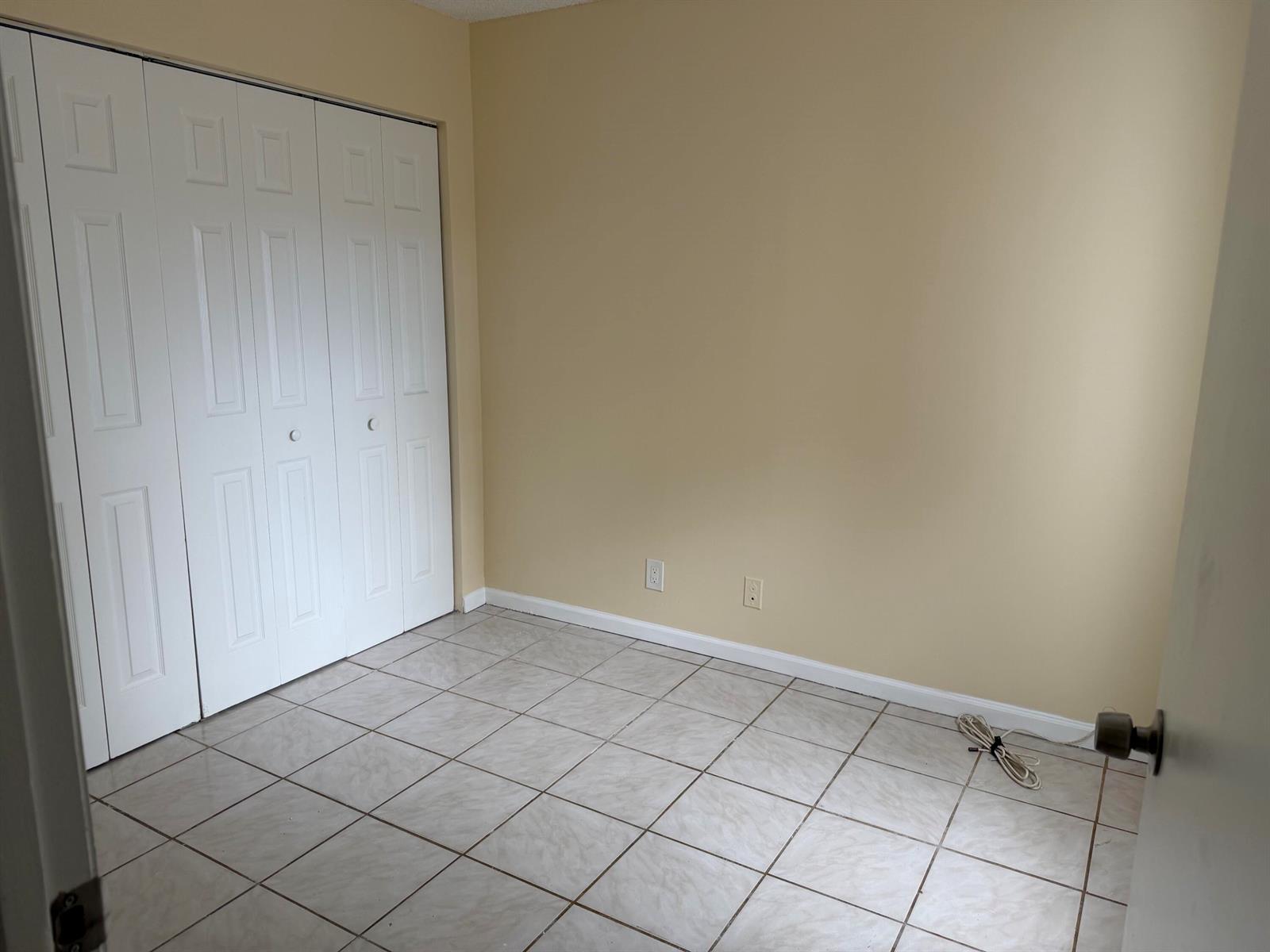 An empty room with beige walls, white bi-fold closet doors, and light-colored tiled flooring — 3730 Village Drive # A, Delray Beach FL 33445, DELRAY BEACH, FL