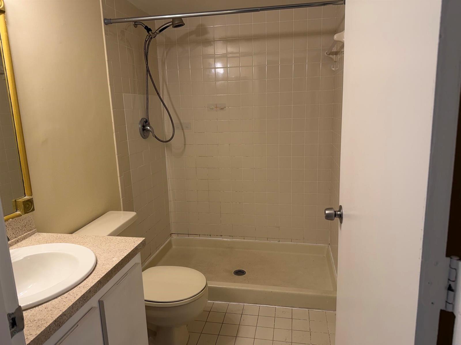 A bathroom features a vanity with a sink, a toilet, and a tiled shower stall — 3730 Village Drive # A, Delray Beach FL 33445, DELRAY BEACH, FL