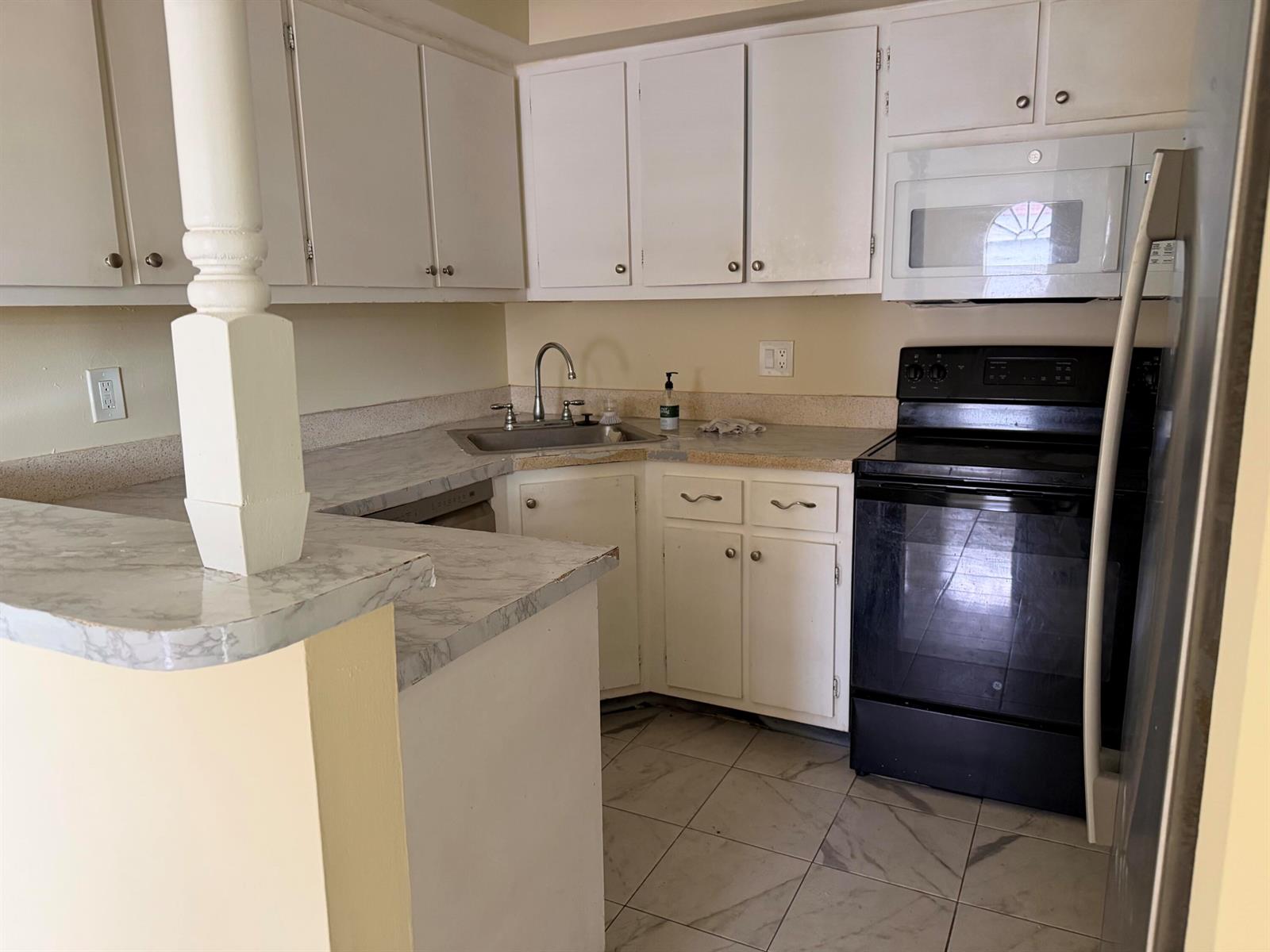 A kitchen features white cabinets, marble-patterned laminate countertops, and black appliances — 3730 Village Drive # A, Delray Beach FL 33445, DELRAY BEACH, FL