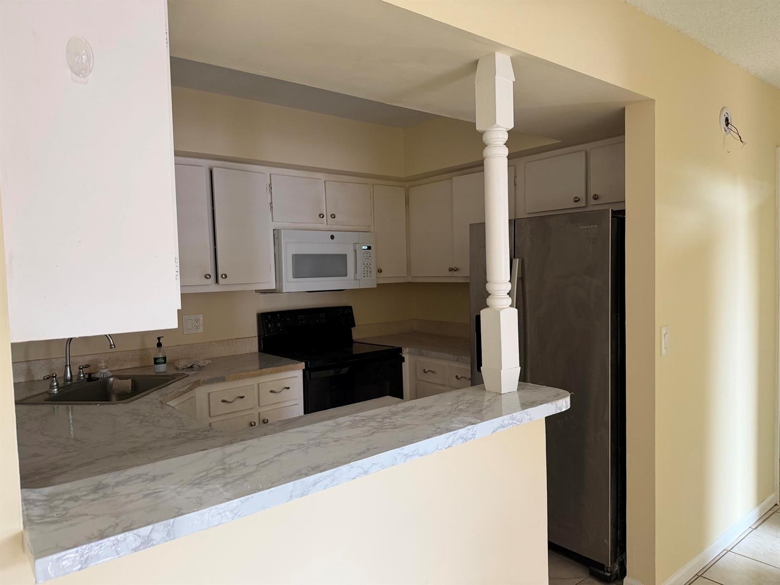 A kitchen features white cabinets, black appliances, a marble-patterned countertop, and a decorative support post — 3730 Village Drive # A, Delray Beach FL 33445, DELRAY BEACH, FL