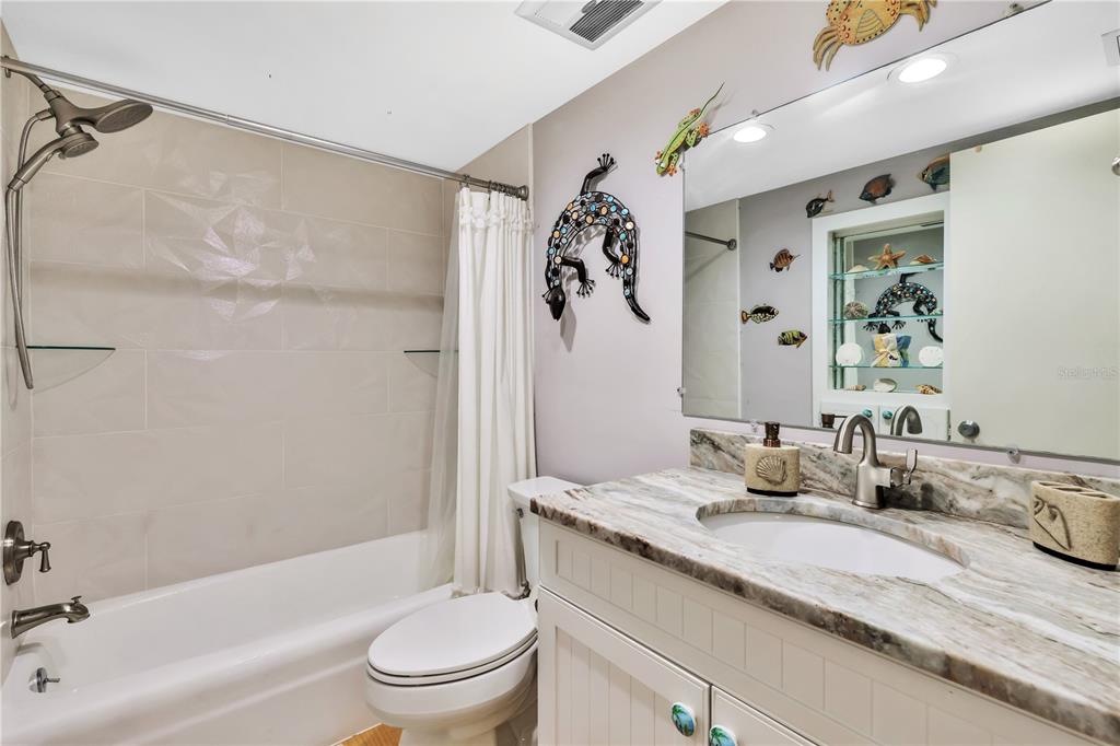 A bathroom features a tub-shower combo, a white vanity with a stone countertop, and nautical decor — 3806 GULF OF MEXICO DR DRIVE UNIT C210, LONGBOAT KEY, FL