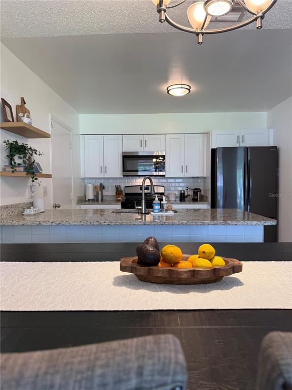 A kitchen features white cabinets, granite countertops, stainless steel appliances, and a wooden fruit bowl — 4808 GANIMEDE LANE, ORLANDO, FL