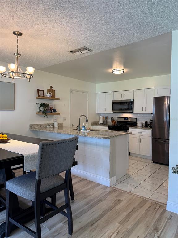 A kitchen with white cabinets, granite countertops, and a dining area with a chandelier — 4808 GANIMEDE LANE, ORLANDO, FL