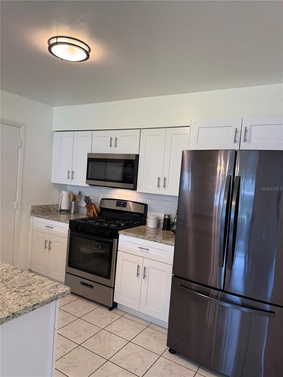 A kitchen features white cabinets, granite countertops, stainless steel appliances, and tile flooring — 4808 GANIMEDE LANE, ORLANDO, FL