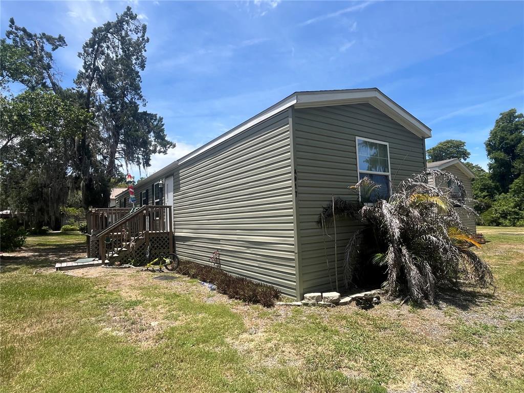 A light green mobile home with a wooden deck and a large palm tree — 4917 ADDESSI LOOP, LAND O LAKES, FL