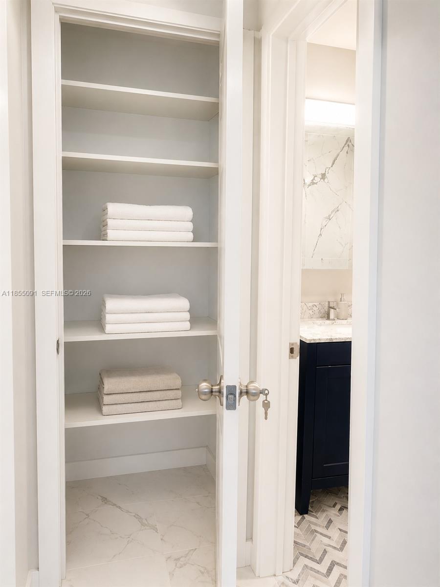 A white linen closet with stacked towels sits next to a bathroom with marble flooring — 5005 Collins Ave # 822, Miami Beach FL 33140, MIAMI BEACH, FL