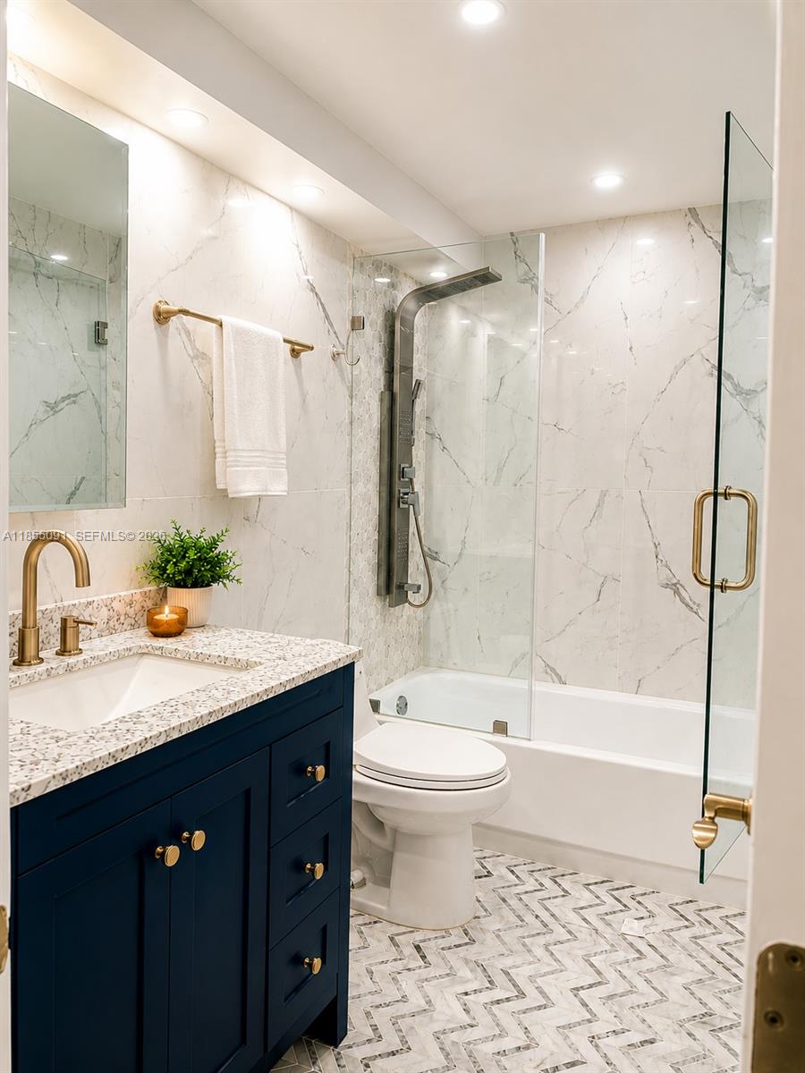 A bathroom features a navy vanity, marble-look tile, a glass-enclosed tub, and chevron floor tiles — 5005 Collins Ave # 822, Miami Beach FL 33140, MIAMI BEACH, FL