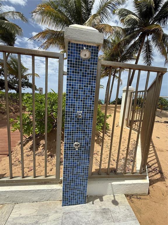 An outdoor shower with blue mosaic tiles stands between metal fence panels near a beach — 968 ROAD LAS  PICUAS UNIT AB 302, RIO GRANDE, PR