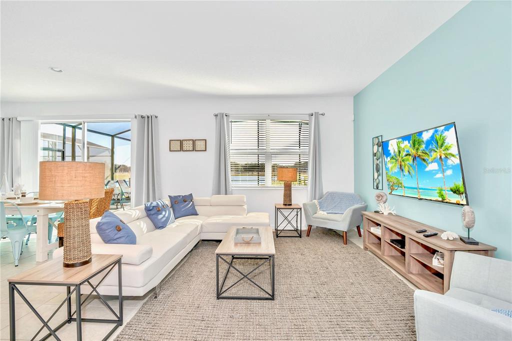 A bright living room features a white sectional sofa, a television, and a light blue wall — 4494 MONADO DRIVE, KISSIMMEE, FL