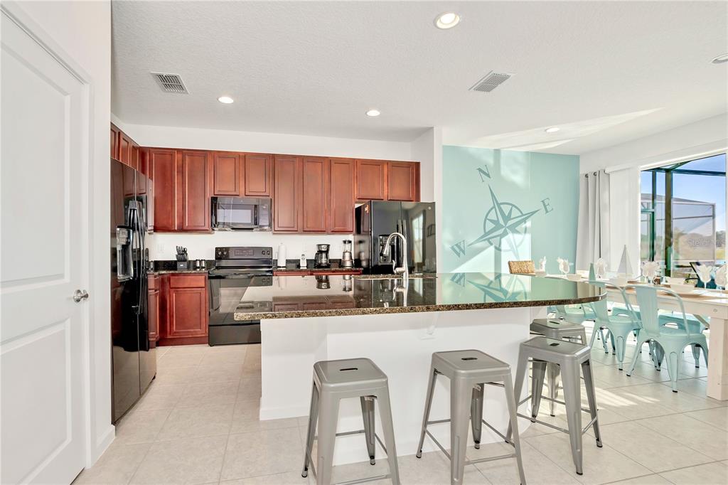A kitchen features dark wood cabinets, granite countertops, a center island, and metal bar stools — 4494 MONADO DRIVE, KISSIMMEE, FL