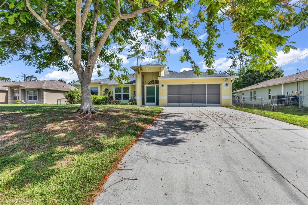 A yellow single-story house with a large tree in the front yard and a driveway — 3660 MADAGASCAR AVENUE, NORTH PORT, FL