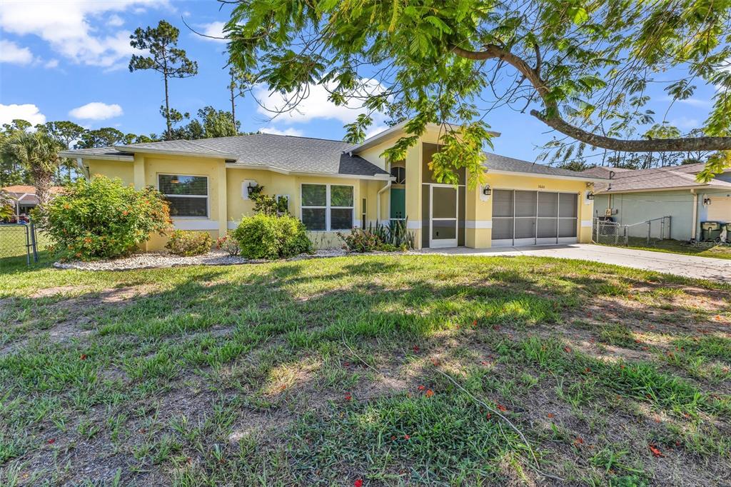 A yellow single-story house with a two-car garage and a front yard with trees — 3660 MADAGASCAR AVENUE, NORTH PORT, FL
