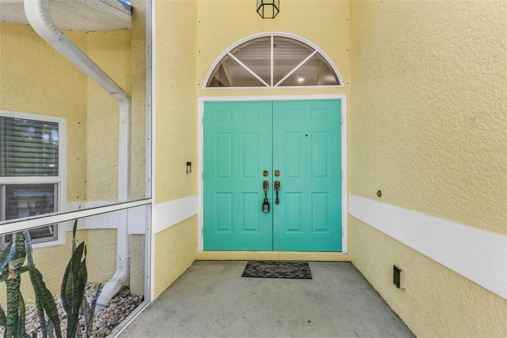 A yellow house exterior features a bright teal double front door with an arched transom window — 3660 MADAGASCAR AVENUE, NORTH PORT, FL