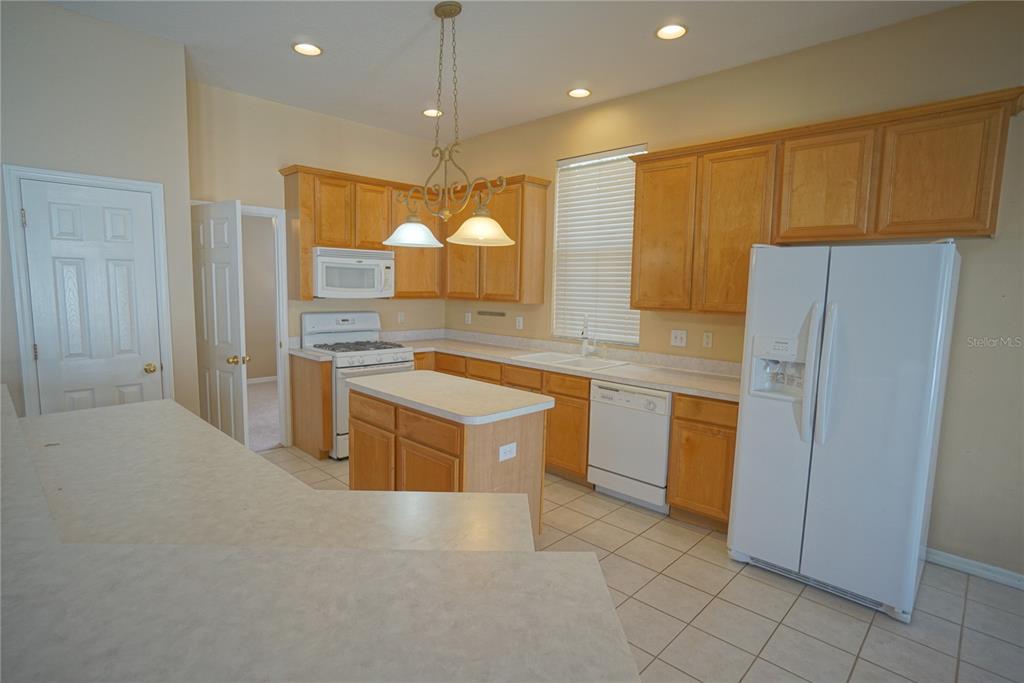 A kitchen features light wood cabinets, white appliances, a central island, and tiled flooring — 12402 WINDMILL COVE DRIVE, RIVERVIEW, FL