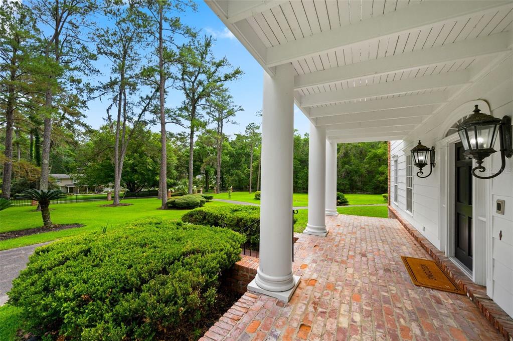 A brick porch with white columns overlooks a large green lawn and tall trees — 7216 NW 20TH PLACE, GAINESVILLE, FL