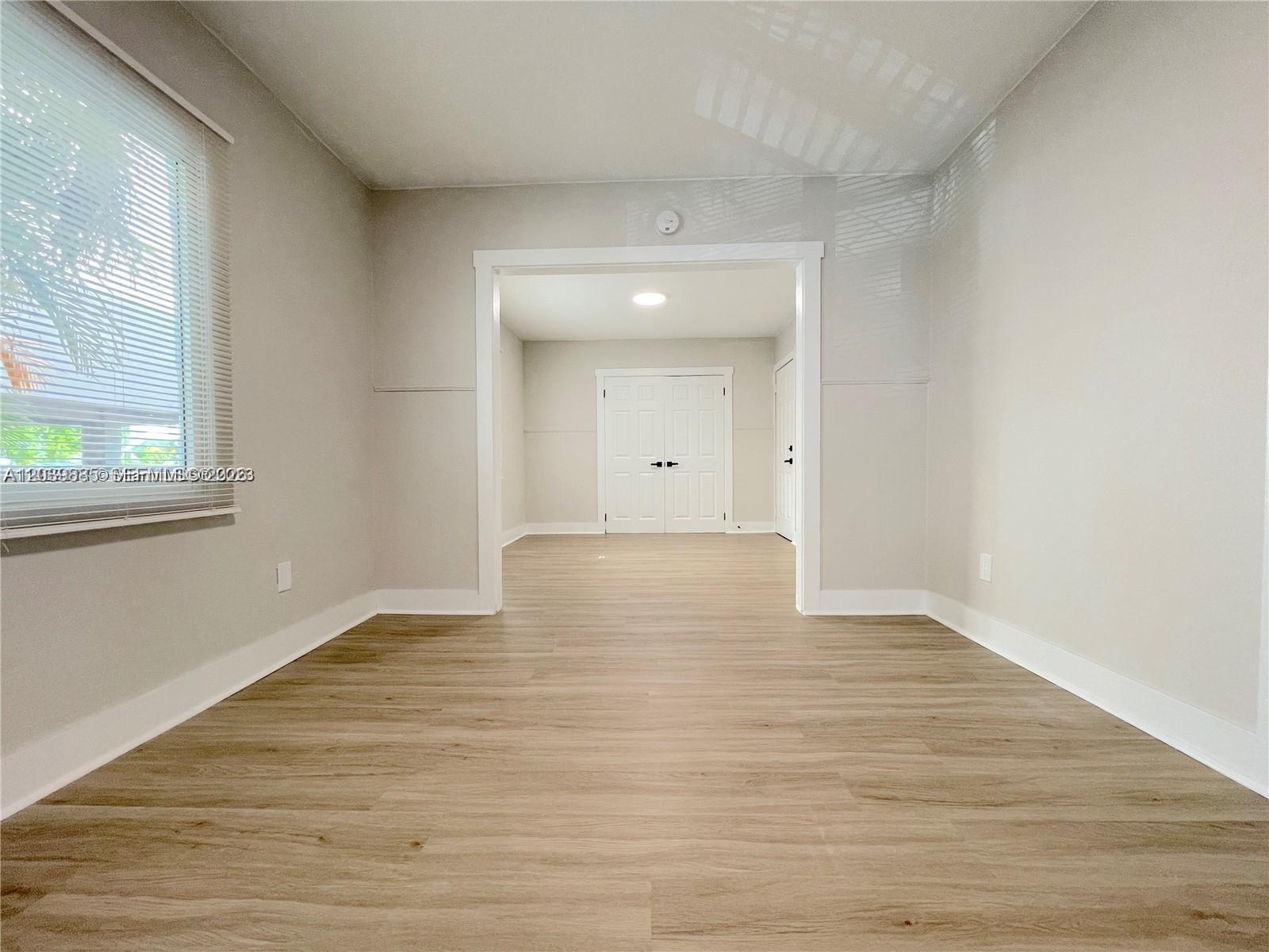 An empty room with light wood-look flooring leads through a doorway to a second space — 1836 Dewey St # 2, Hollywood FL 33020, HOLLYWOOD, FL