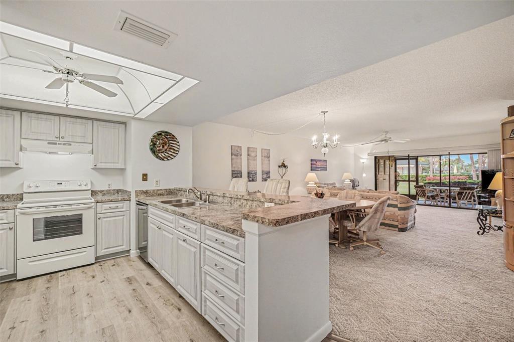 A kitchen with white cabinets and granite countertops overlooks a carpeted dining and living area — 601 SHREVE STREET UNIT 66A, PUNTA GORDA, FL