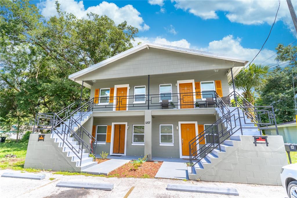 A two-story apartment building with exterior staircases, orange doors, and gray siding — 1207 W CYPRESS STREET, ORLANDO, FL