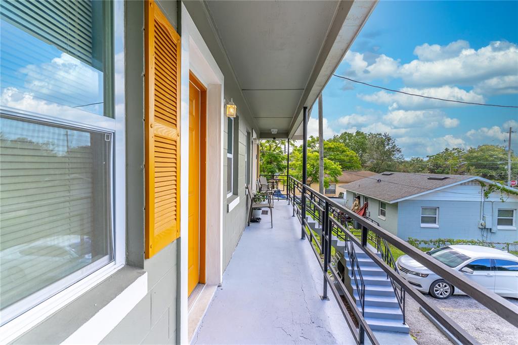 An outdoor balcony with a yellow door, metal railing, and stairs leading to a parking area — 1207 W CYPRESS STREET, ORLANDO, FL