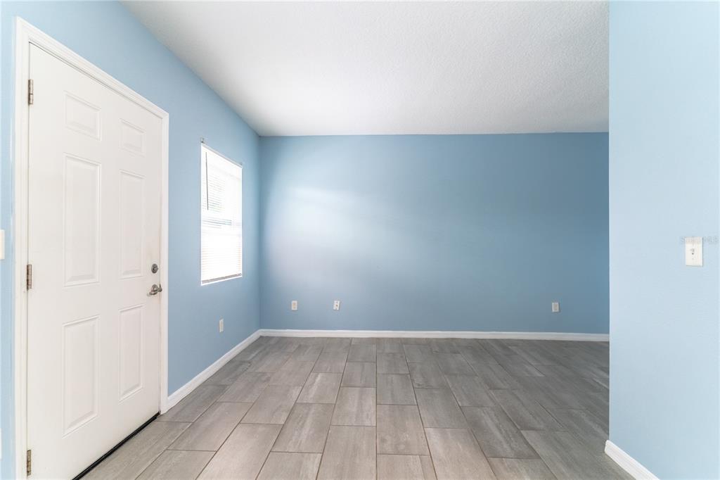 An empty room with light blue walls, gray tile flooring, and a white entry door — 1207 W CYPRESS STREET, ORLANDO, FL