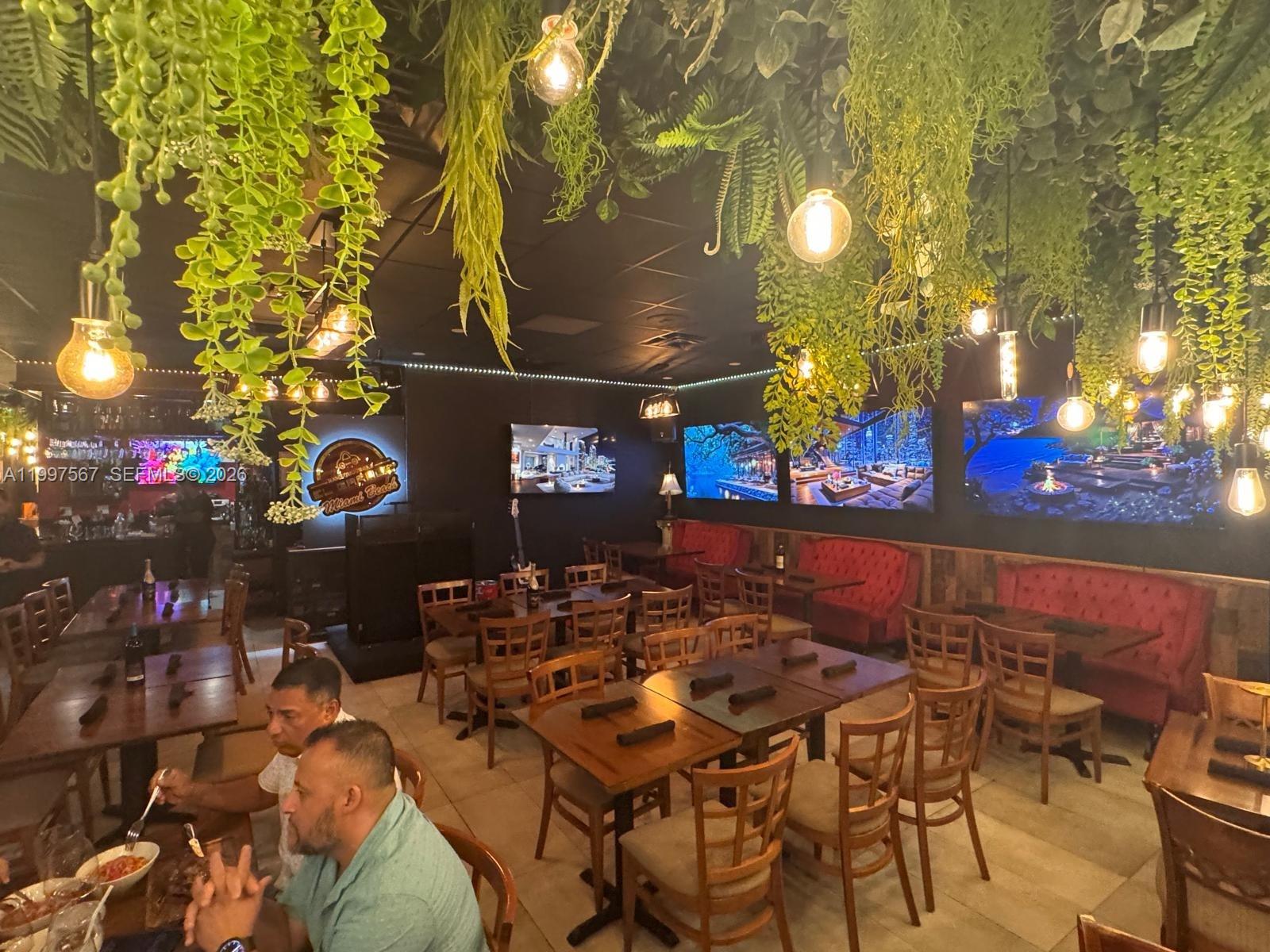 A restaurant dining area features wooden tables, chairs, red booths, and hanging greenery — 946 Normandy Dr, Miami Beach FL 33141, MIAMI BEACH, FL