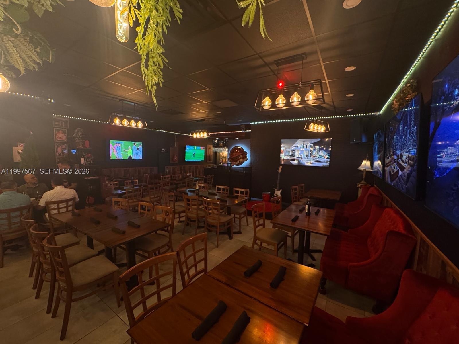 A dimly lit restaurant interior features wooden tables, chairs, red booths, and wall-mounted televisions — 946 Normandy Dr, Miami Beach FL 33141, MIAMI BEACH, FL