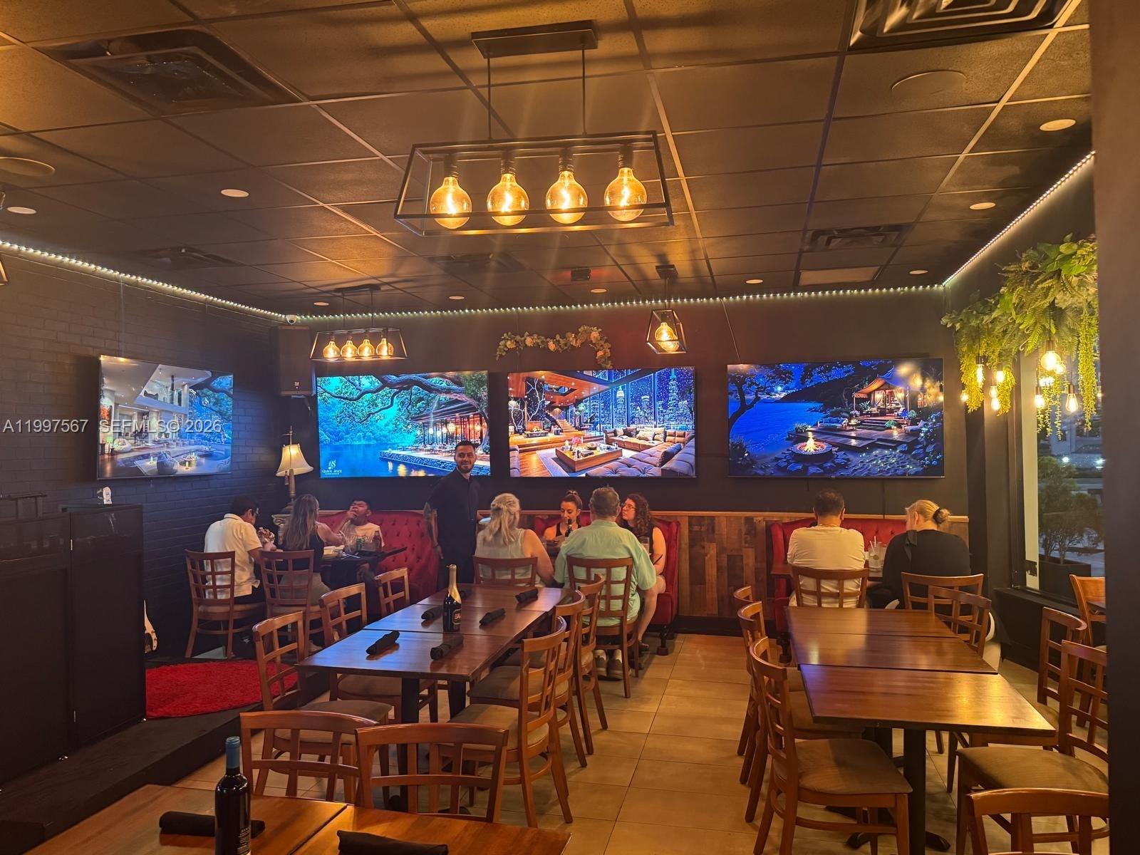 A restaurant interior features wooden tables, chairs, dark walls, and multiple screens displaying scenic images — 946 Normandy Dr, Miami Beach FL 33141, MIAMI BEACH, FL
