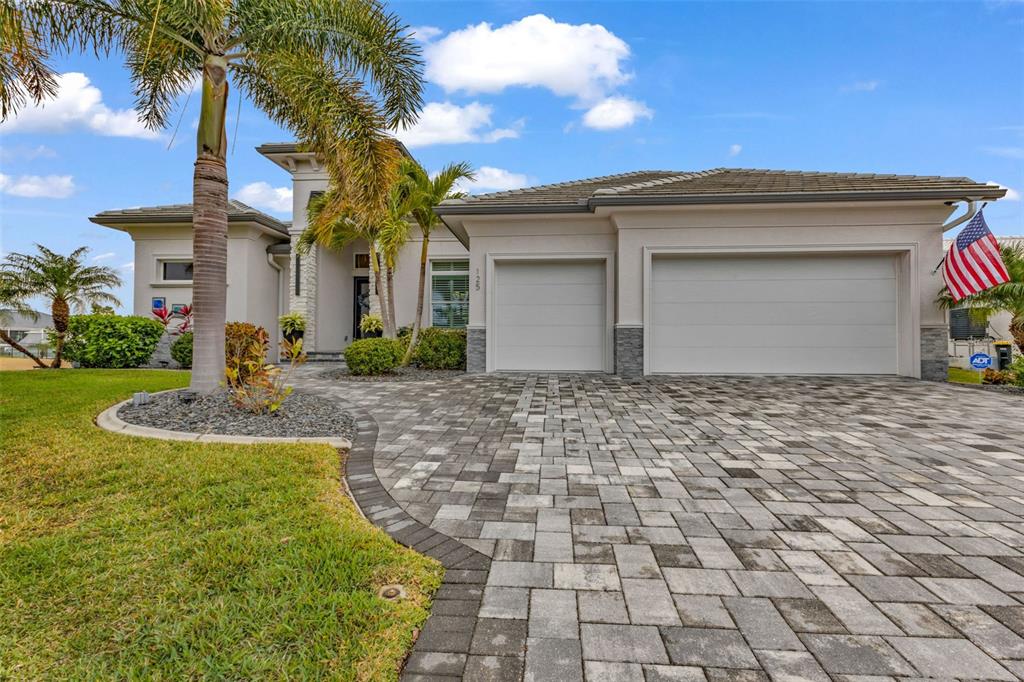 A single-story house with a paved driveway, three-car garage, and palm trees under a blue sky — 125 GREAT ISAAC COURT, PUNTA GORDA, FL