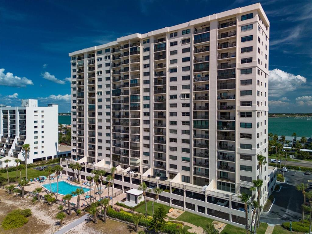 A tall, multi-story residential building with balconies stands next to a swimming pool and beach — 1270 GULF BOULEVARD UNIT 1503, CLEARWATER BEACH, FL