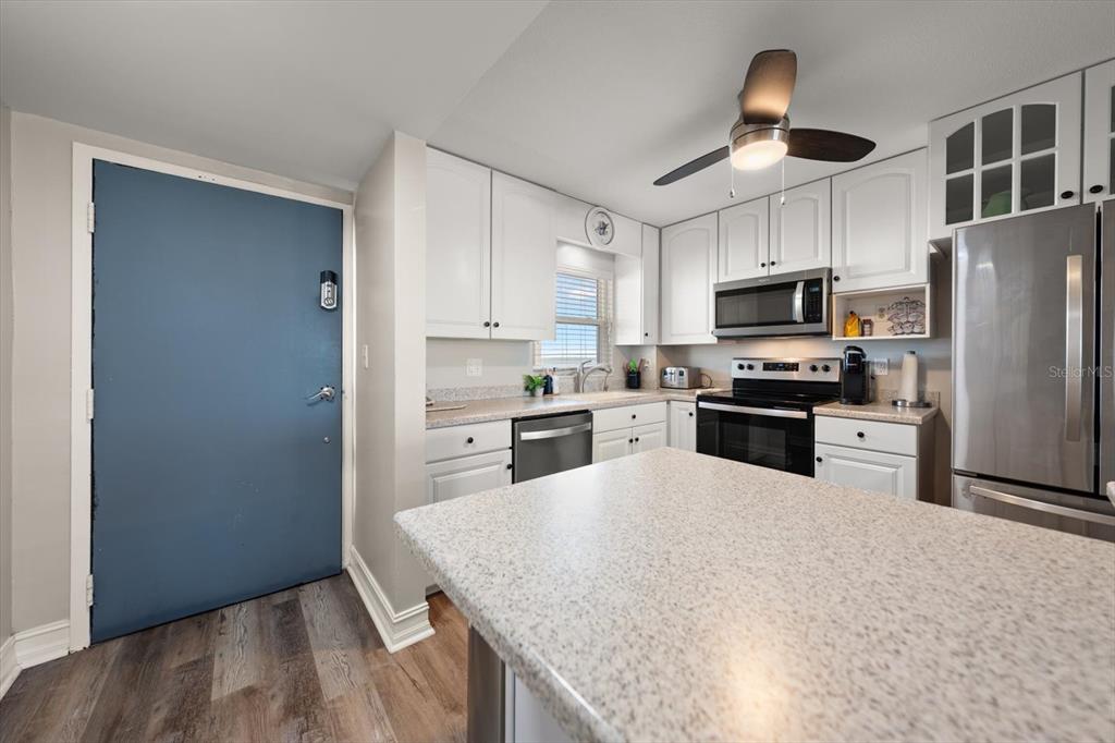 A kitchen features white cabinets, stainless steel appliances, a speckled countertop, and a blue door — 1270 GULF BOULEVARD UNIT 1503, CLEARWATER BEACH, FL