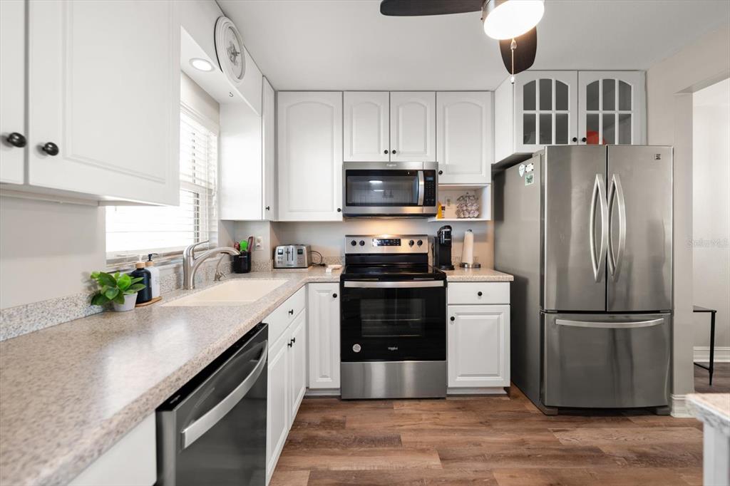 A kitchen features white cabinets, stainless steel appliances, speckled countertops, and wood-look flooring — 1270 GULF BOULEVARD UNIT 1503, CLEARWATER BEACH, FL