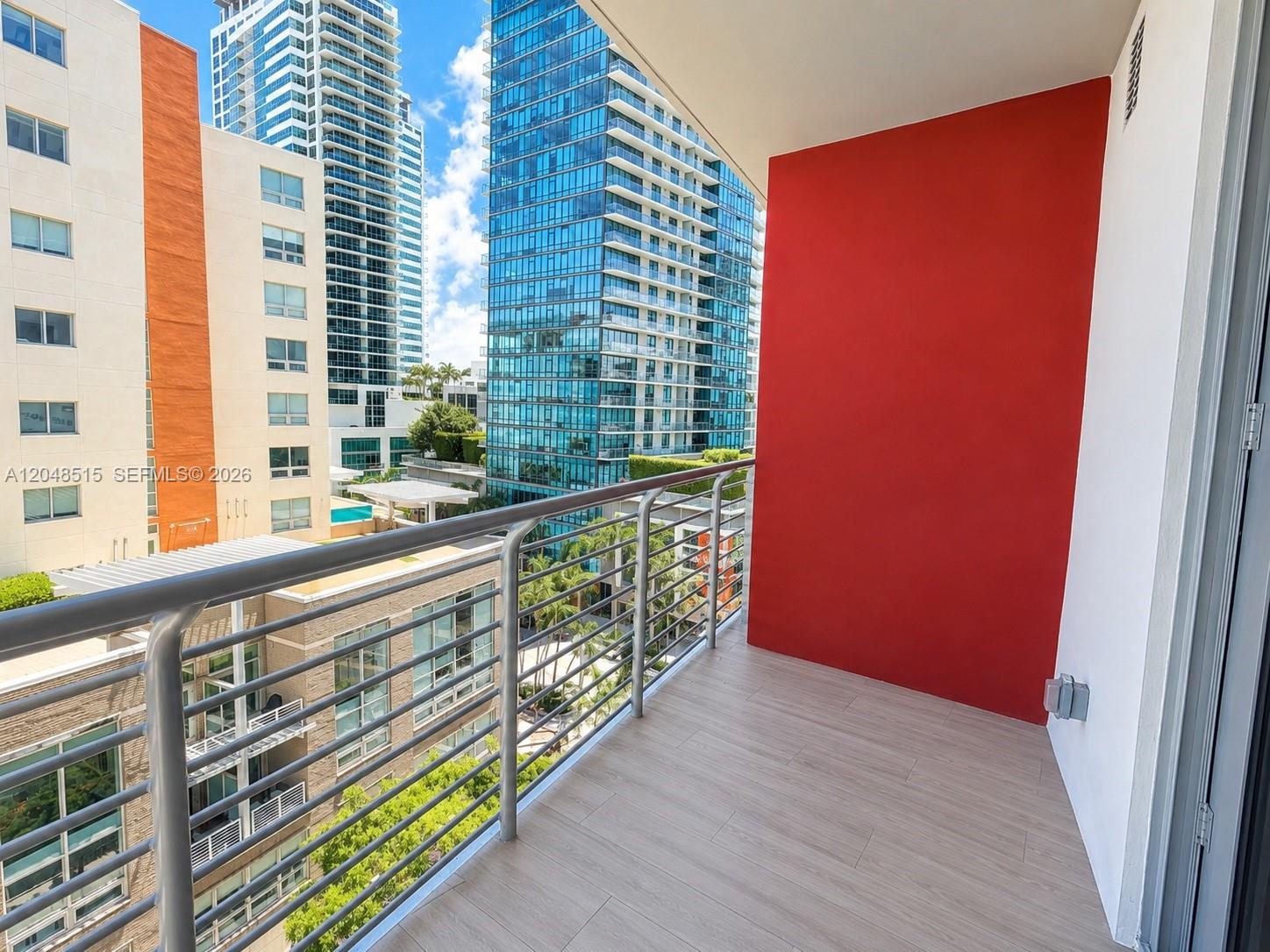 A balcony with wood-look tile flooring, a metal railing, and a bright red accent wall — 90 NE 32nd St # 814, Miami FL 33137, MIAMI, FL