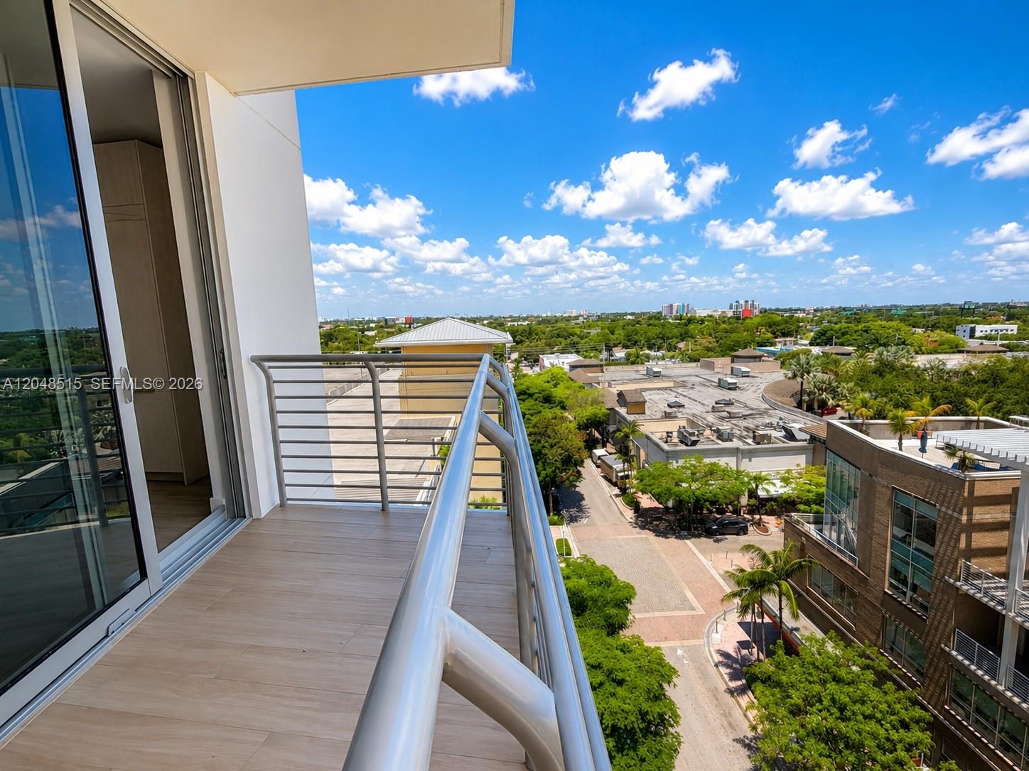 A balcony with a metal railing overlooks a street, trees, and buildings under a sky — 90 NE 32nd St # 814, Miami FL 33137, MIAMI, FL