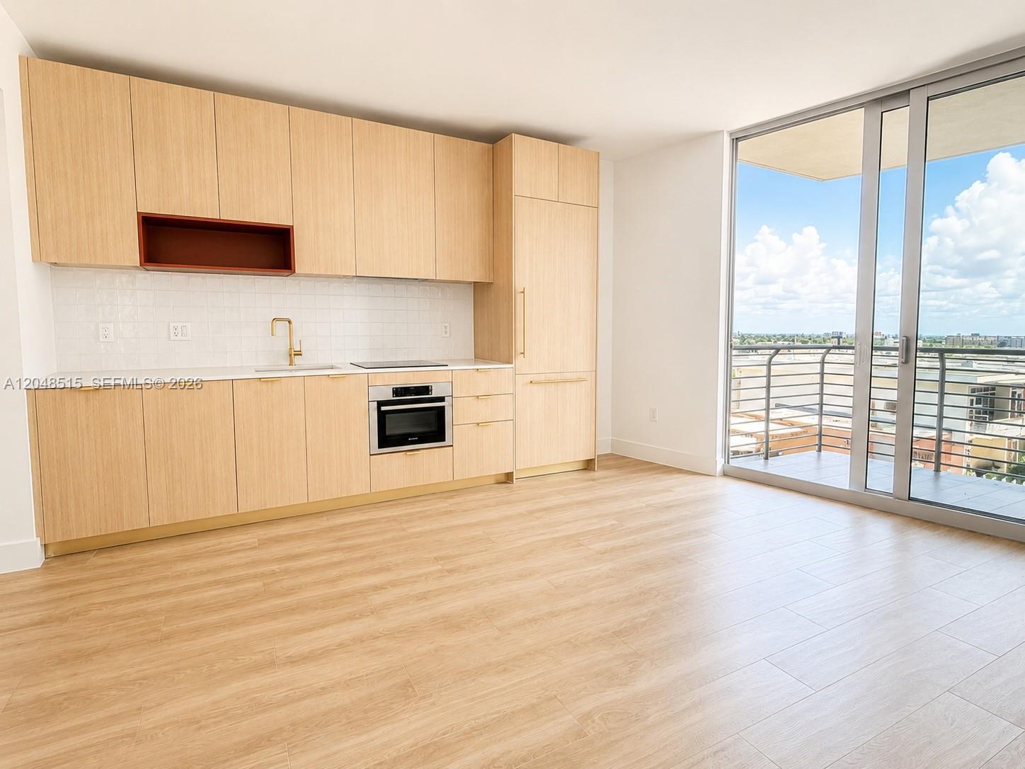 A modern kitchen with light wood cabinetry and a balcony overlooking a city skyline — 90 NE 32nd St # 814, Miami FL 33137, MIAMI, FL