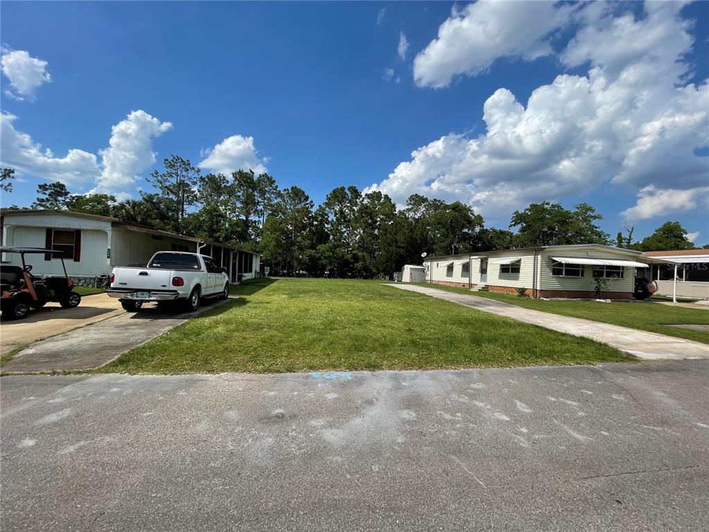 A vacant grassy lot sits between two manufactured homes with driveways on a sunny day — 162 LEISURE WORLD DRIVE N, DEBARY, FL