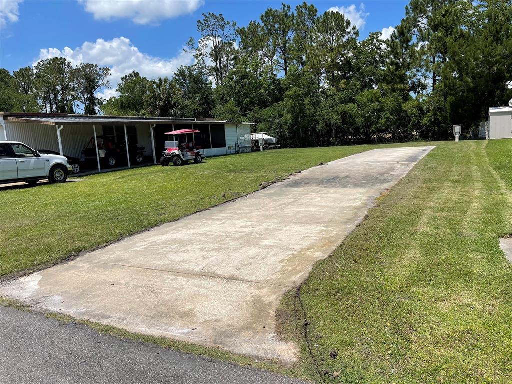 A long concrete driveway extends toward a house with a carport and a golf cart — 162 LEISURE WORLD DRIVE N, DEBARY, FL