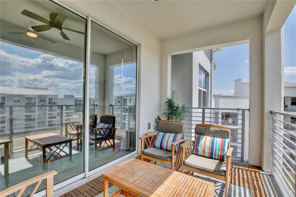 A covered balcony features wooden furniture, striped cushions, and a view of neighboring apartment buildings — 3180 PARADOX CIRCLE UNIT 402, KISSIMMEE, FL