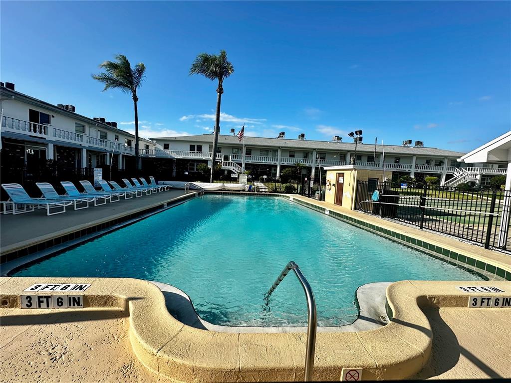 A rectangular swimming pool is surrounded by lounge chairs and a multi-story apartment building — 4742 AZALEA DRIVE UNIT 205, NEW PORT RICHEY, FL
