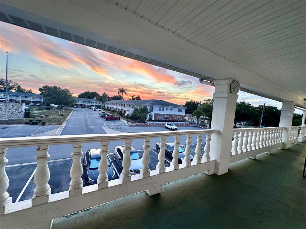 A covered balcony with a white balustrade overlooks a parking lot at sunset — 4742 AZALEA DRIVE UNIT 205, NEW PORT RICHEY, FL