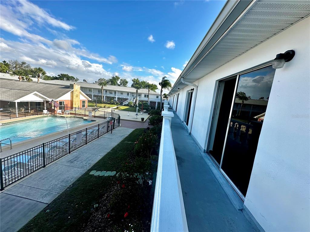 An exterior balcony overlooks a swimming pool and a multi-story apartment building — 4742 AZALEA DRIVE UNIT 205, NEW PORT RICHEY, FL
