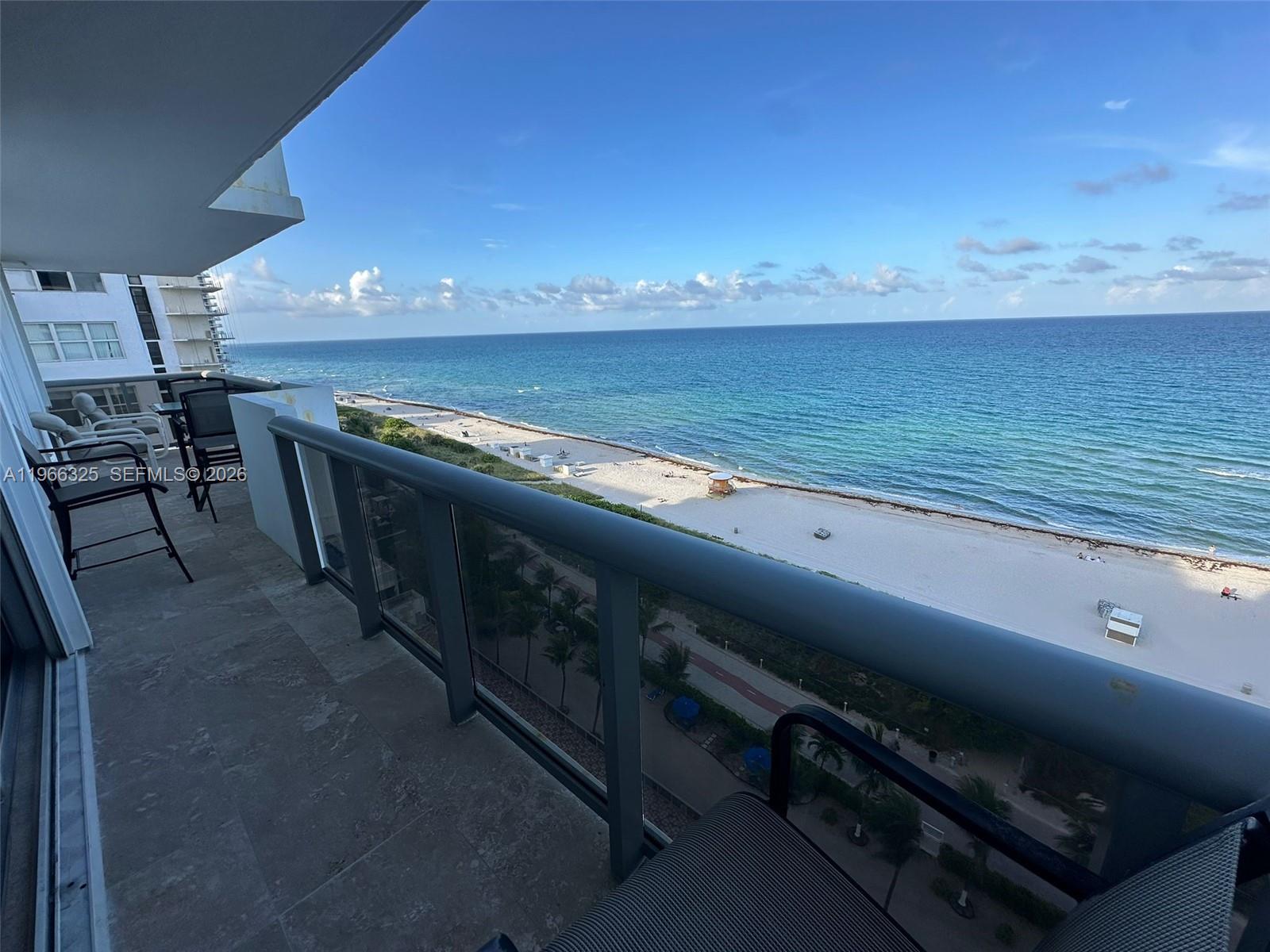 A high-rise balcony overlooks a sandy beach and the ocean on a sunny day — 6039 Collins Ave # 1517, Miami Beach FL 33140, MIAMI BEACH, FL