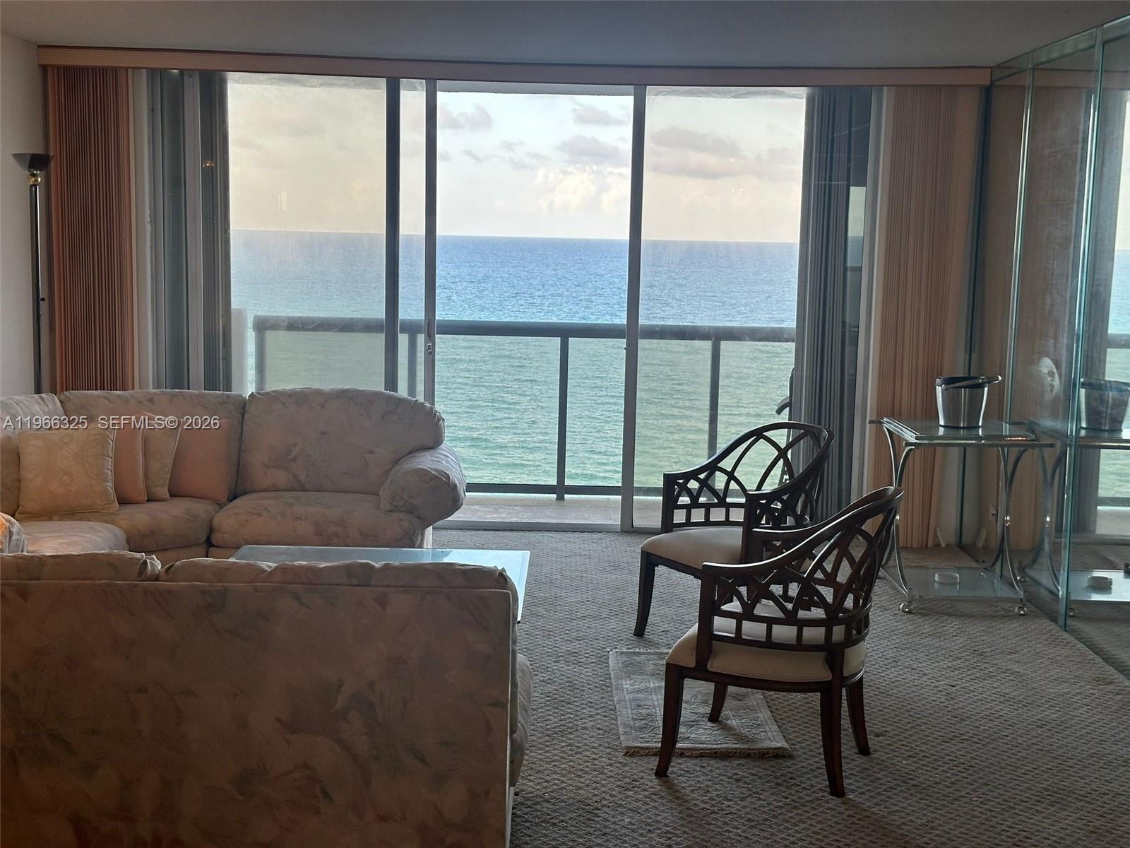 A living room features a floral sofa, two patterned chairs, and a balcony overlooking the ocean — 6039 Collins Ave # 1517, Miami Beach FL 33140, MIAMI BEACH, FL