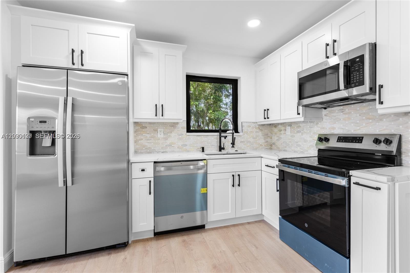 A kitchen features white cabinetry, stainless steel appliances, a tiled backsplash, and light wood flooring — 14171 SW 37th Ct, Davie FL 33330, DAVIE, FL