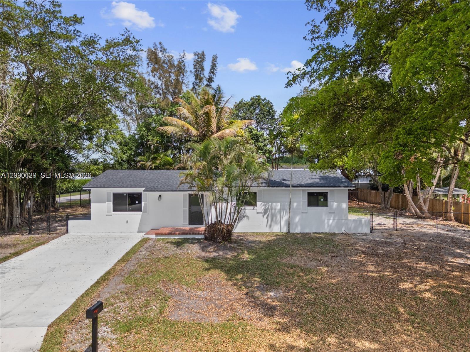 A white, single-story house with a dark roof sits on a lot with trees — 14171 SW 37th Ct, Davie FL 33330, DAVIE, FL